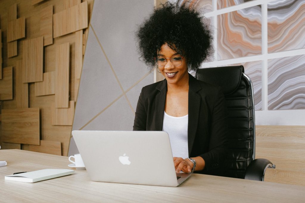 woman in black blazer sitting by the table while using macbook, woman making money online by using perpetual income 365 perhaps